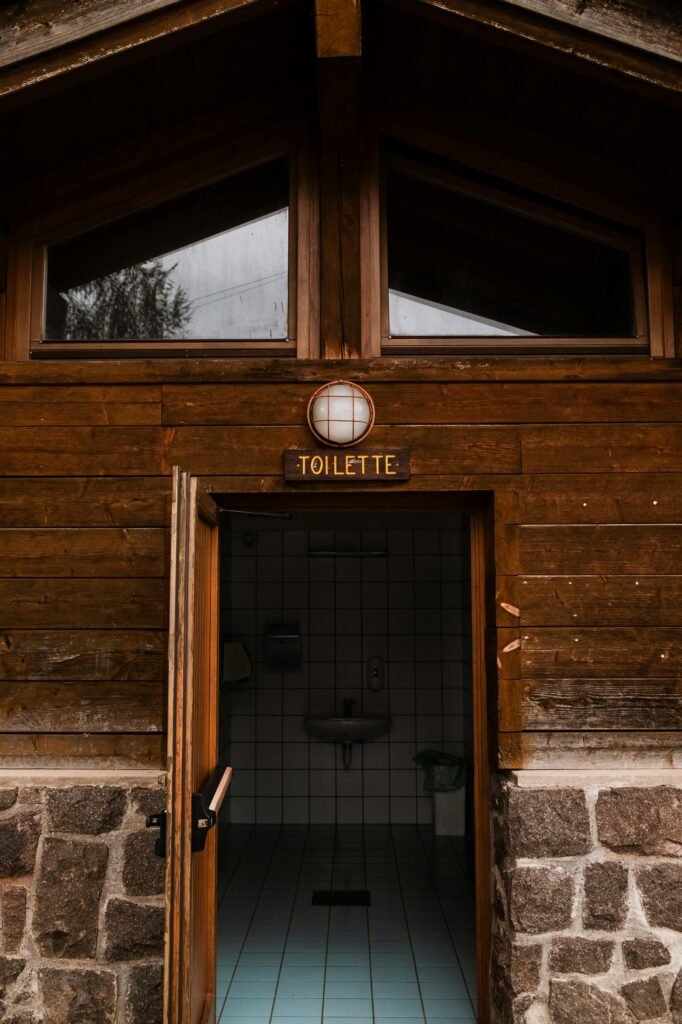 A rustic wooden exterior of a public restroom with an open door showing tiled interior.