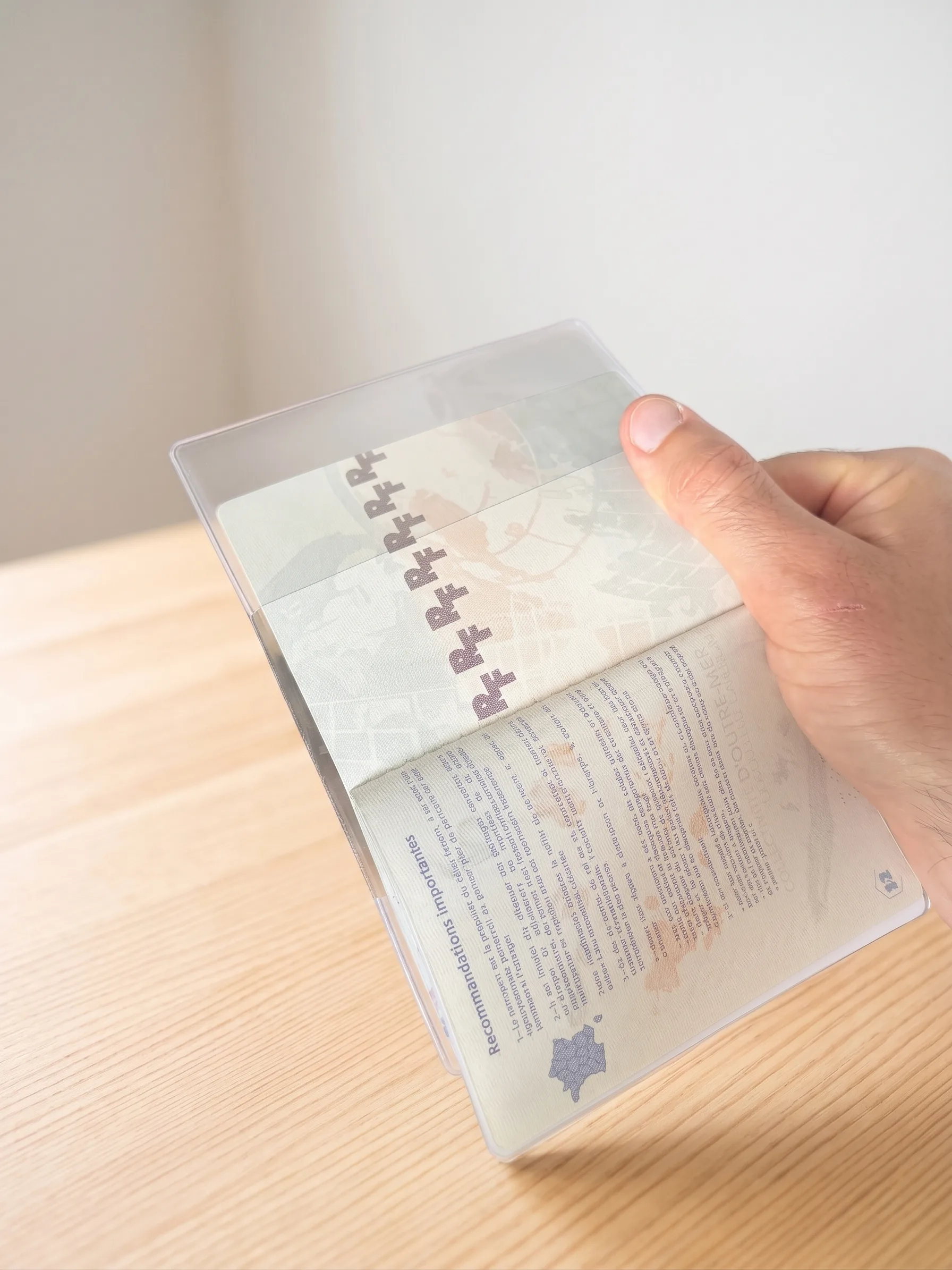 Passeport ouvert dans un étui transparent Habeygard® tenu à la main sur une table claire